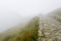 Silhouettes of a group of people in thick fog on a rocky hiking trail in the mountains