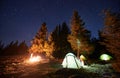 Team of friends resting in campsite on hill under starry sky by campfire. Royalty Free Stock Photo