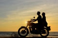 Silhouettes of guy and girl on motorcycle on ocean sunset background. Young couple are sitting on motorcycle, faces in profile