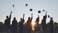 Silhouettes of Happy college graduates tossing their caps up at sunset.