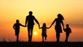 Silhouettes of happy family holding the hands in the meadow during sunset. Royalty Free Stock Photo