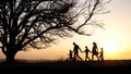 Silhouettes of happy family walking together in the meadow during sunset Royalty Free Stock Photo