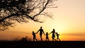 Silhouettes of happy family walking together in the meadow during sunset