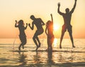 Silhouettes of happy friends jumping inside water on the beach at sunset - Group of young people having fun on summer vacation - Royalty Free Stock Photo