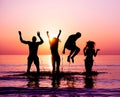 Silhouettes of happy friends jumping inside water on the beach at sunset - Group of young people having fun on summer vacation - Royalty Free Stock Photo