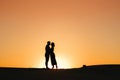 Silhouettes of a happy young couple on a background of orange sunset in the sand desert