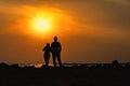 Silhouettes of man and woman on a dais stand with their backs and look at sea sunset