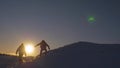 Silhouettes of men descending from high snowy mountain seeking adventure in glare of setting sun in winter. Concept of