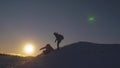Silhouettes of men descending from high snowy mountain seeking adventure in glare of setting sun in winter. Concept of