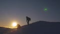 Silhouettes of men descending from high snowy mountain seeking adventure in glare of setting sun in winter. Concept of