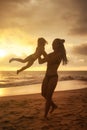 Silhouettes of mother and little girl daughter playing fun on beach at sunset sky background Royalty Free Stock Photo
