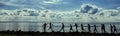 Silhouettes of newlyweds with guests walking along the rocky shore against the background of the beach