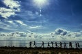 Silhouettes of newlyweds with guests walking along the rocky shore against the background of the beach, sea and sky