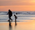 Silhouettes in the sunset at the beach: grandpa playing soccer with his grandson in the shallow water