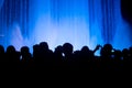 Silhouettes of people in a crowd watching a light water show at night with classic blue color background