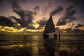 Silhouettes of people next to the sailboat on the shore with the sunset in the cloudy background Royalty Free Stock Photo