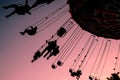 Silhouettes of people on swing carousel against purple evening sky