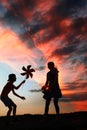 Silhouettes of playing boy with windmill and girl with ball in the nature in red blue dramatic cloudy sky background