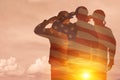 Silhouettes of soldiers with print of sunset and USA flag saluting on a background of light sky.