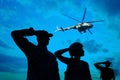 Silhouettes of soldiers in uniform saluting and military helicopter