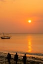 Silhouettes of three Masai in traditional clothes standing on the beach, during orange sunset, with calm sea view, Zanzibar