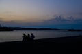Silhouettes of three people sitting near the sea against a sunset