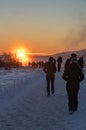 Silhouettes of tourists walking in single file along a completely snow-covered path towards the Strokkur geyser with the sun