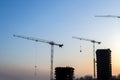 Silhouettes of tower cranes constructing a new residential building at a construction site against sunset background. Renovation Royalty Free Stock Photo