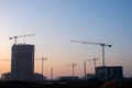 Silhouettes of tower cranes constructing a new residential building at a construction site against sunset background. Renovation Royalty Free Stock Photo