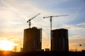 Silhouettes of tower cranes constructing a new residential building at a construction site against sunset background. Renovation Royalty Free Stock Photo