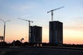 Silhouettes of tower cranes constructing a new residential building at a construction site against sunset background. Renovation Royalty Free Stock Photo