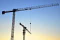 Silhouettes of tower cranes constructing a new residential building at a construction site against sunset background. Renovation Royalty Free Stock Photo