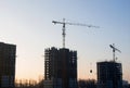 Silhouettes of tower cranes constructing a new residential building at a construction site against sunset background. Renovation Royalty Free Stock Photo