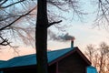 Silhouettes of trees and a fragment of a house with thick smoke coming from the chimney