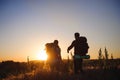 Silhouettes of two hikers with backpacks walking at sunset. Trekking and enjoying the sunset view.