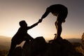 Silhouettes of two people climbing on mountain and helping. Help and assistance concept. Silhouette of Teamwork on the mountains