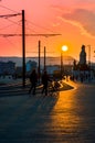 Silhouettes of two persons walking with bicycle down the pedestrian street in back light of spectacular sunset of evening Budapest