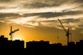 The silhouettes of two tower cranes and houses during sunset, sunset with an orange sky in the city Royalty Free Stock Photo