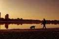 Silhouettes of a woman walking with a dog along the lake at sunset Royalty Free Stock Photo