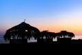 Silhouettes of wooden hovels covered with reeds and palm leaves on the beach at sunset