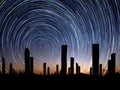 Silhouettes of wooden pillars with circle star trail in blue and orange sky, long exposure