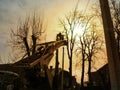 Silhouettes of workers pruning tall trees with an aerial work platform in the golden rays of the sun. The concept of work on the Royalty Free Stock Photo