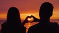 Silhouettes of a young couple, hands show the shape of the heart against the backdrop of the sunset over the sea Royalty Free Stock Photo