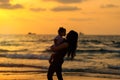 Silhouettes young mother with daughter playing and kissing on the beach at sunset evening sky background. Happy family.