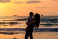 Silhouettes young mother with daughter playing and kissing on the beach at sunset evening sky background. Happy family.