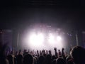 Silhouettes of young people with the raised hands up before a scene at a concert. Rock group. Bright light on the stage