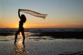 Silhoutte of a pretty senior Asian female in a swimming suit standing and flaunt yellow fabric on the beach. Royalty Free Stock Photo