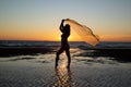 Silhoutte of a pretty senior Asian female in a swimming suit standing and flaunt yellow fabric on the beach. Royalty Free Stock Photo