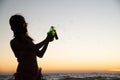 Silhoutte of a pretty senior Asian female in a swimming suit standing and hold sprashing water gun posing on the beach. Royalty Free Stock Photo