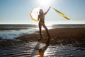 Silhoutte of a pretty senior Asian female in a swimming suit standing and hold umbrella and flaunt yellow fabric on the beach. Royalty Free Stock Photo